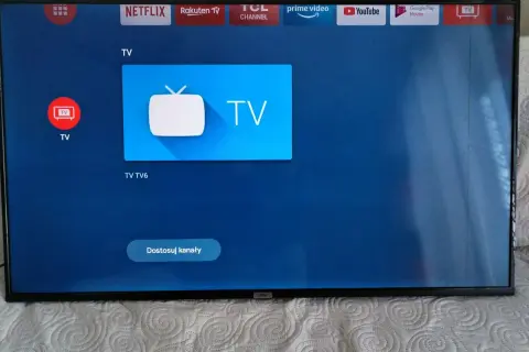 Ekran telewizora z ikonami aplikacji, w tym Netflix i YouTube. Widoczne są czarne paski po bokach.