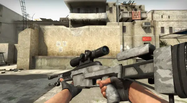 Gracz trzyma karabin snajperski Scout w CS:GO, gotowy do akcji na pustynnej mapie.