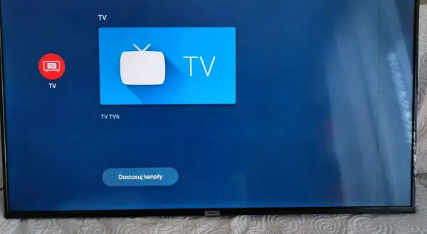 Ekran telewizora z ikonami aplikacji, w tym Netflix i YouTube. Widoczne są czarne paski po bokach.