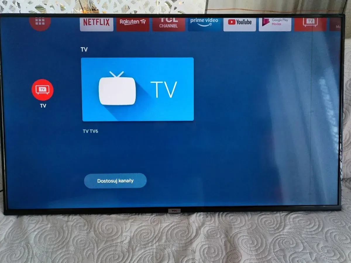 Ekran telewizora z ikonami aplikacji, w tym Netflix i YouTube. Widoczne są czarne paski po bokach.