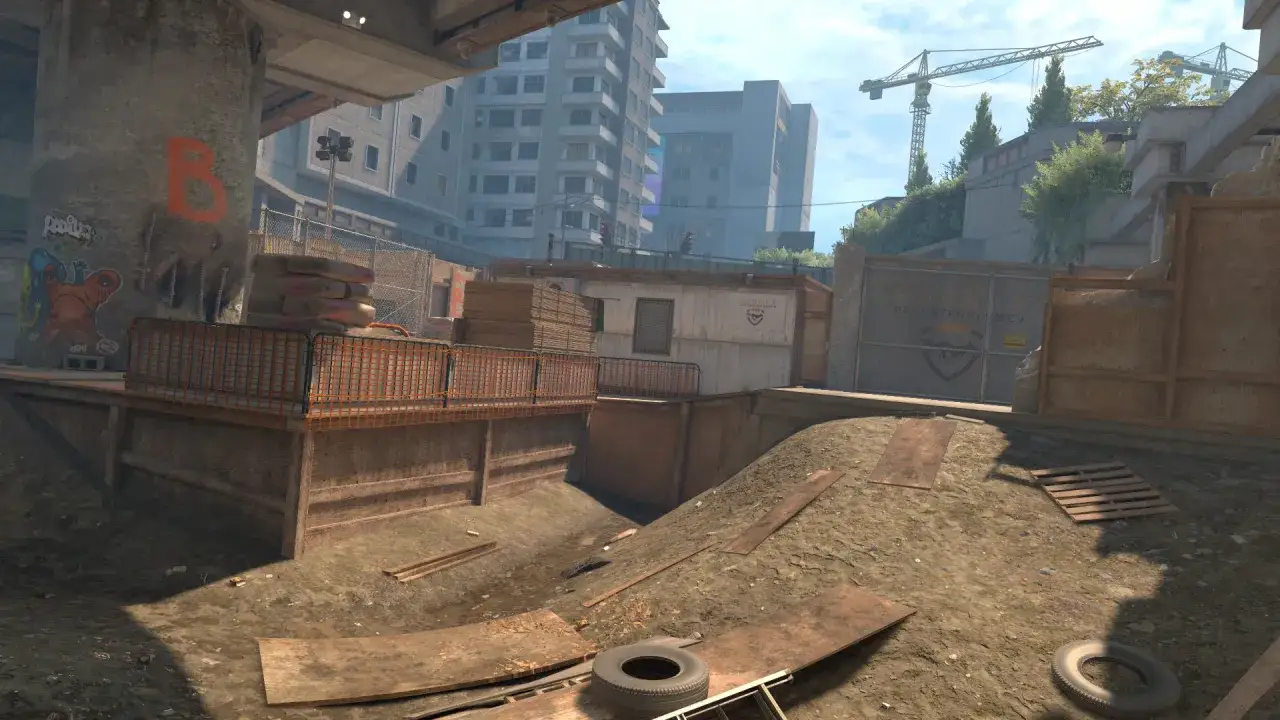 Plac budowy z elementami CS GO workshop: betonowy filar z graffiti, worki z cementem, budynki w tle, dźwigi.