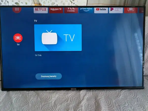 Ekran telewizora z ikonami aplikacji, w tym Netflix i YouTube. Widoczne są czarne paski po bokach.